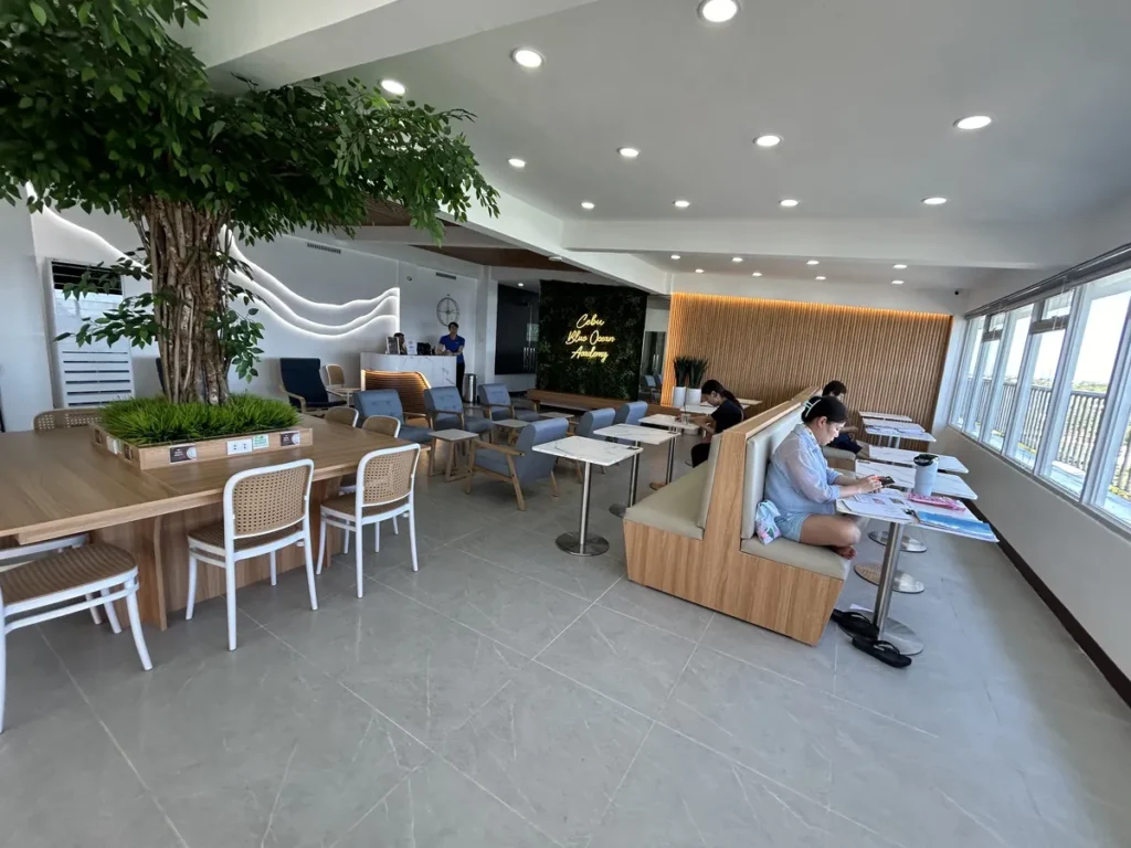 필리핀 세부 블루오션(BLUEOCEAN) 어학원 라운지로 노란 사인 간판과 부스형 좌석, 대리석 테이블이 배치된 학생 카페테리아 공간입니다