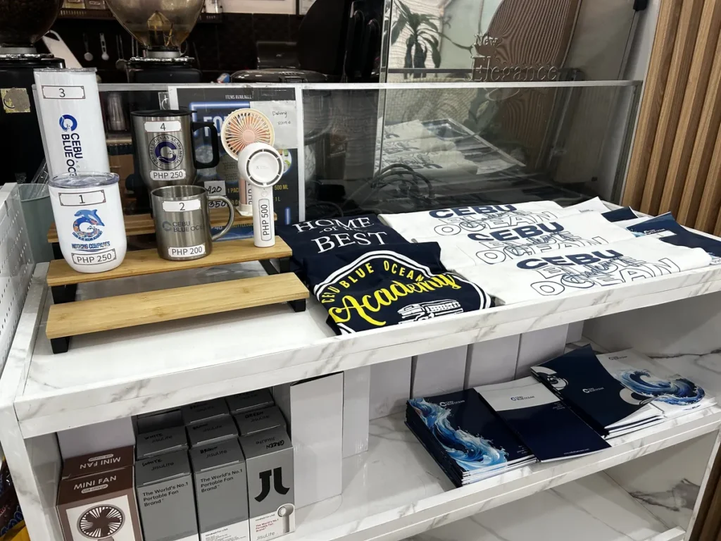 필리핀 세부 블루오션(BLUEOCEAN) 어학원 매점 진열대에 텀블러, 학원 로고 티셔츠, 미니 선풍기 굿즈를 진열한 모습