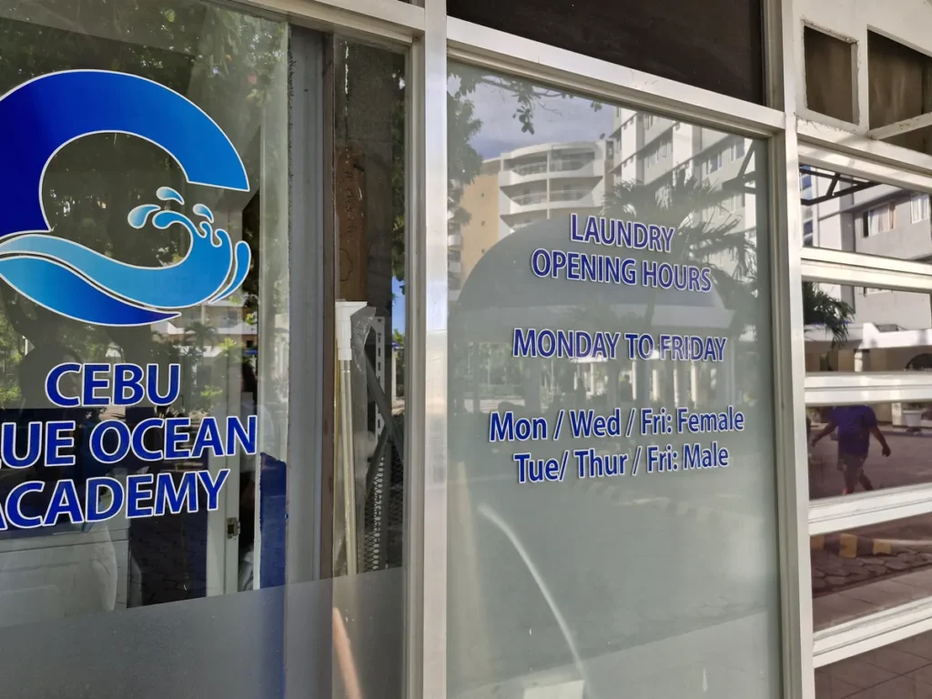 필리핀 세부 블루오션(BLUEOCEAN) 어학원 부대시설 세탁실 유리창에 적힌 로고와 요일별 운영 시간 안내