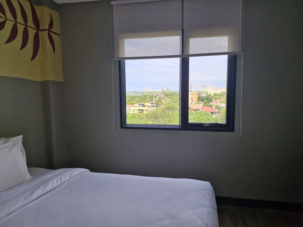 필리핀 세부 블루오션(BLUEOCEAN) 어학원 외부숙소 1인실 슈페리어 침대 옆 창문으로, 멀리 주택가와 도심 풍경이 펼쳐집니다.
