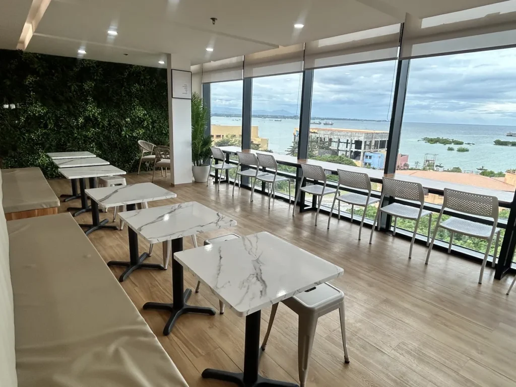필리핀 세부 블루오션(BLUEOCEAN) 어학원 외부숙소 옥상 루프덱으로, 유리 난간 너머 바다와 항구가 보이는 긴 테이블의 야외 좌석입니다.