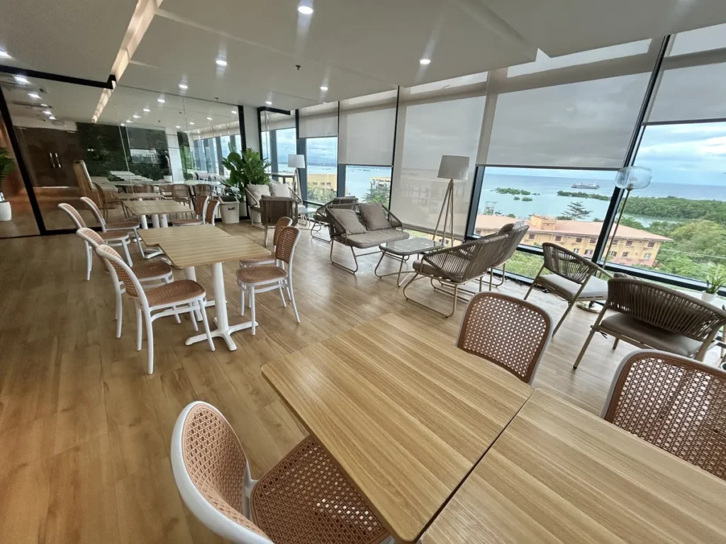 필리핀 세부 블루오션(BLUEOCEAN) 어학원 외부숙소 부대시설로, 통창 너머 바다 전망을 마주한 라탄 의자와 검정 테이블의 다이닝 공간입니다.