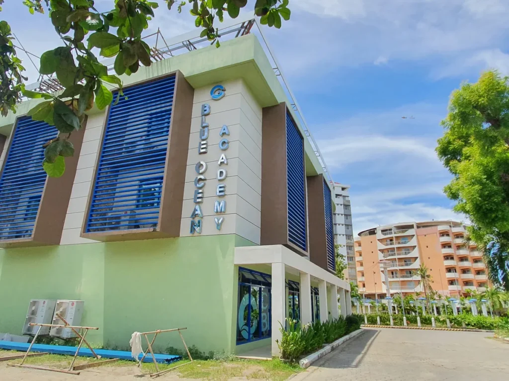 필리핀 세부 블루오션(BLUEOCEAN) 어학원 BLUE OCEAN ACADEMY 간판이 붙은 건물 외관과 야자수, 야외 좌석이 있는 진입로