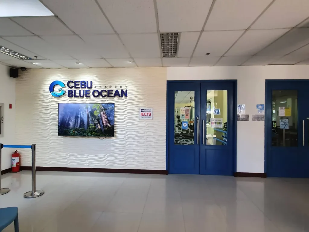 필리핀 세부 블루오션(BLUEOCEAN) 어학원 입구홀 벽면의 CEBU BLUE OCEAN 로고 사인과 IELTS 등록센터 안내, 파란 출입문