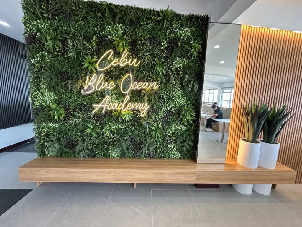 필리핀 세부 블루오션(BLUEOCEAN) 어학원 입구홀 벽면의 Cebu Blue Ocean Academy 그린월 사인과 원목 선반, 화분 장식