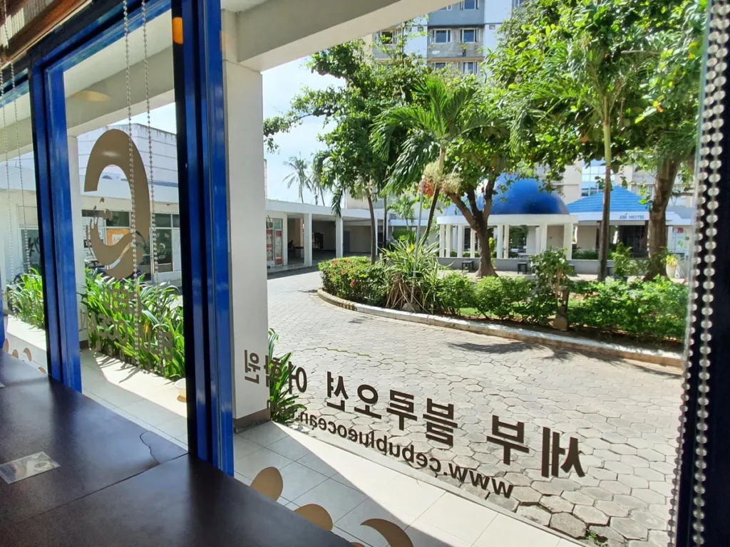 필리핀 세부 블루오션(BLUEOCEAN) 어학원 유리문 안에서 바라본 야자수 안뜰과 한글 안내판