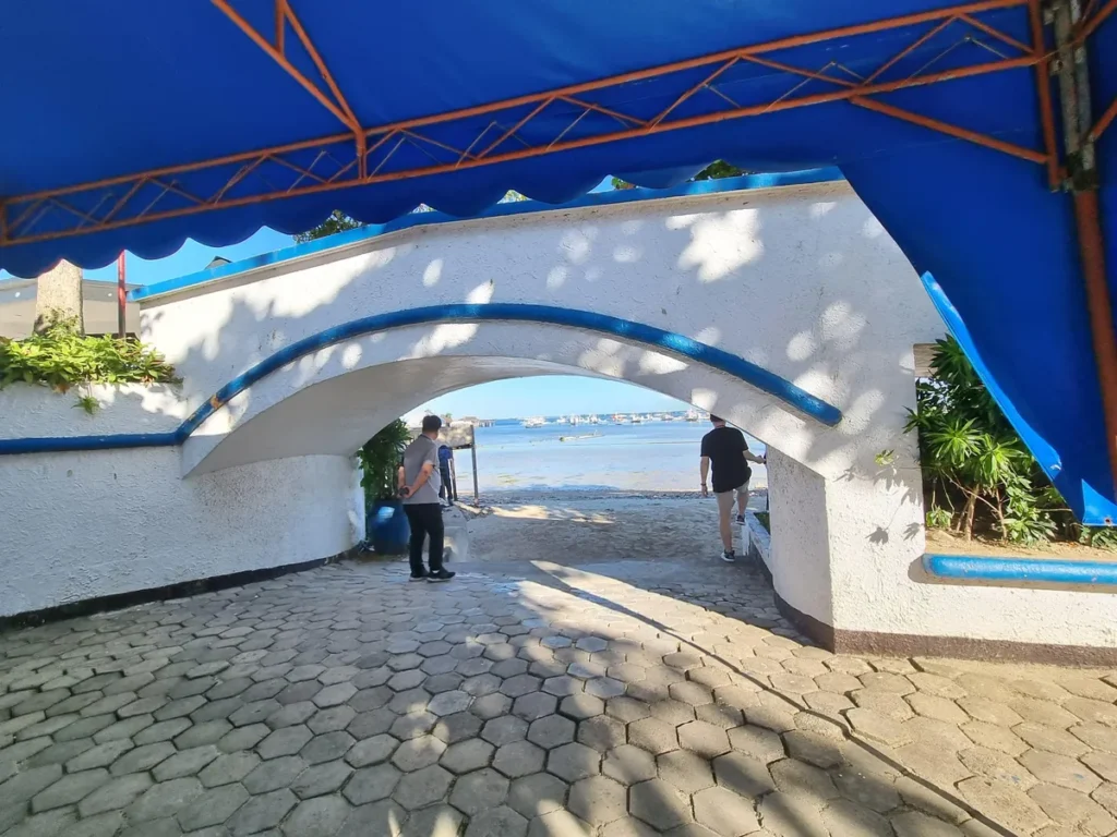 필리핀 세부 블루오션(BLUEOCEAN) 어학원 파란 차양 아래 흰색 아치 통로 너머로 해변과 바다가 보입니다