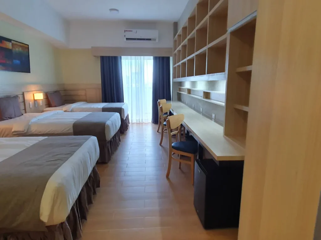 필리핀 세부 CIA어학원 3인실로 침대들과 함께 벽면을 따라 긴 책상과 수납 선반이 배치되어 있습니다.