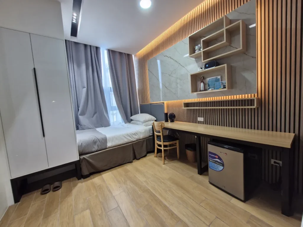 필리핀 세부 CIA어학원 피나클 1인실 내부로 흰색 옷장과 싱글 침대, 책상과 의자, 소형 냉장고가 우드 바닥 위에 배치되어 있다