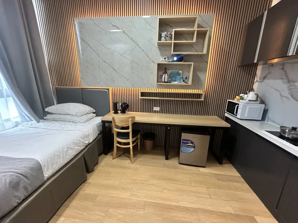 필리핀 세부 CIA어학원 외부숙소 피나클 1인실 전경으로 싱글 침대와 긴 책상, 대리석 장식벽과 우드 선반, 소형 냉장고가 한눈에 들어온다