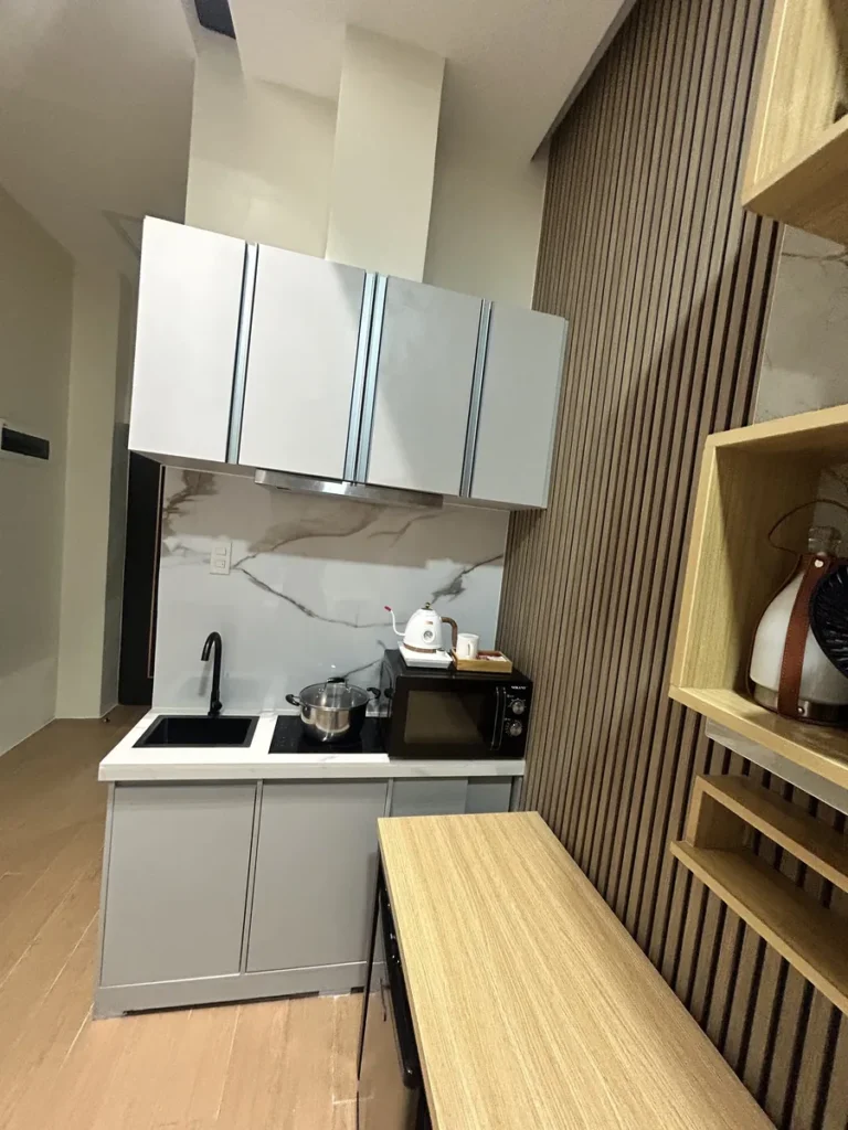 필리핀 세부 CIA어학원 피나클 1인실 주방 클로즈업으로 회색 상부장과 싱크대, 인덕션 위 냄비, 전기포트와 전자레인지가 놓여 있다