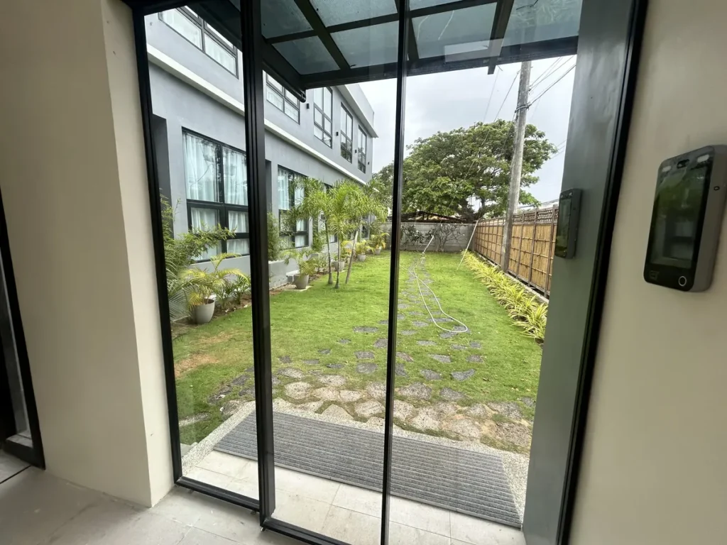 필리핀 세부 CIA어학원 외부기숙사 외관, 실내 통유리문 너머로 잔디 정원과 건물 측면이 내다보이는 모습