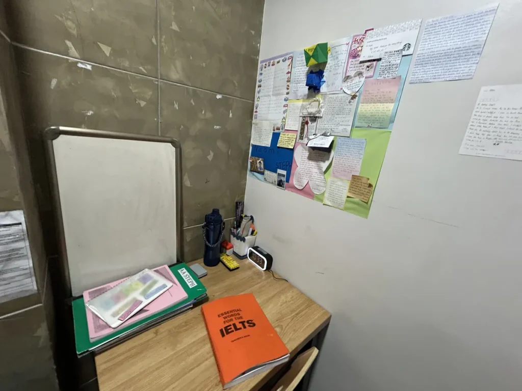 필리핀 세부 CIA어학원 1대1 수업실, 화이트보드와 학습 게시물을 둔 부스 책상에 IELTS 교재가 놓여 있습니다.