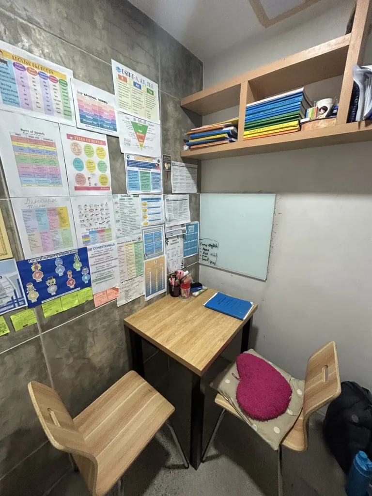 필리핀 세부 CIA어학원 1대1 수업실, 벽면 학습 포스터와 선반, 화이트보드를 갖춘 작은 책상 부스입니다.