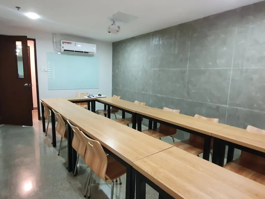 필리핀 세부 CIA어학원 그룹 강의실, 출입문 옆 유리 화이트보드와 벽걸이 에어컨이 설치된 ㄷ자 책상 교실입니다.