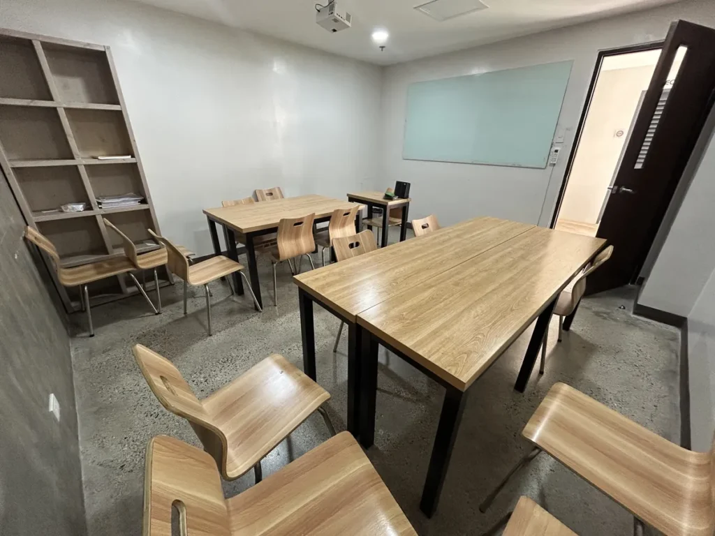 필리핀 세부 CIA어학원 그룹 강의실, 한쪽 벽 책장과 통창이 있는 밝은 교실에 원목 책상이 배치돼 있습니다.