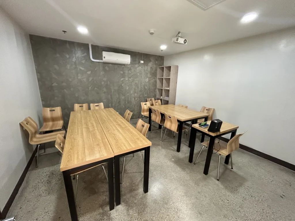 필리핀 세부 CIA어학원 그룹 강의실, 벽면 책장과 유리 화이트보드를 갖춘 교실에 책상 여러 개를 모아 두었습니다.