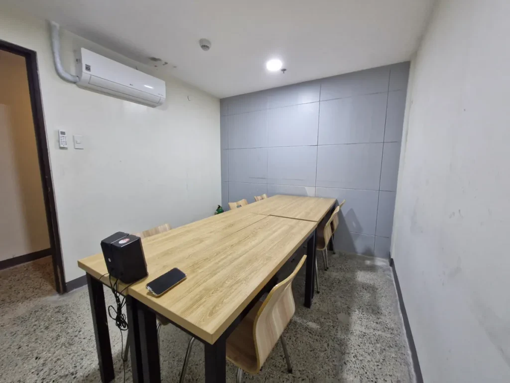 필리핀 세부 CIA어학원 그룹 강의실, 회색 타일 벽 앞에 원목 책상을 길게 붙이고 의자를 둘러 배치한 교실입니다.