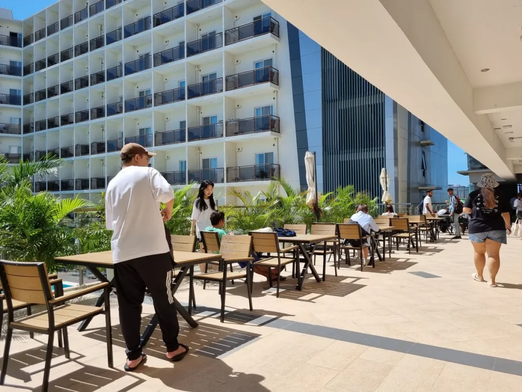 필리핀 세부 CIA어학원 라운지 및 카페, 햇살 아래 건물 옆 야외 통로에 테이블이 늘어서고 학생들이 오가는 모습