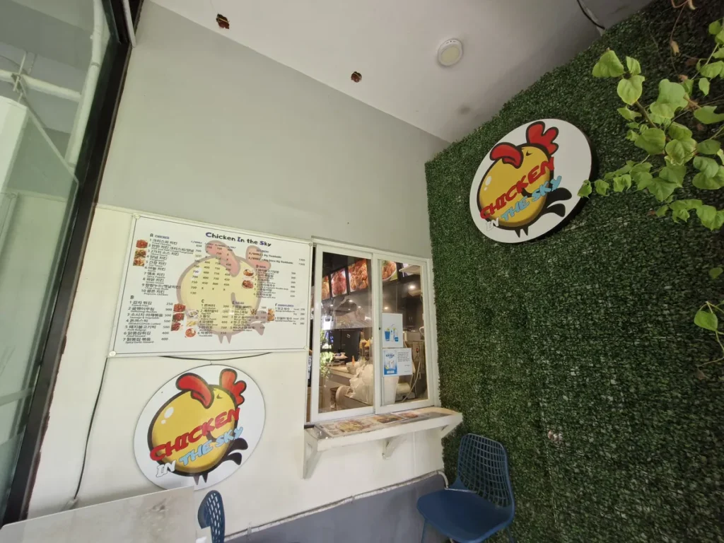 필리핀 세부 CIA어학원 치킨인더스카이 매장 외부 메뉴판과 인조잔디 벽의 로고 간판 모습