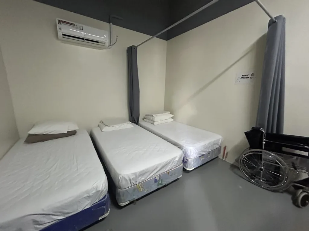 필리핀 세부 CIA어학원 의무실 안정실로, 흰 시트를 깐 침대 세 개가 나란히 놓여 있고 한쪽 구석에 휠체어가 비치되어 있습니다.