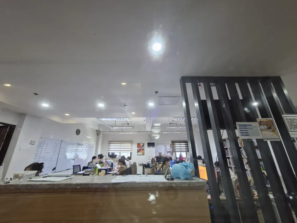 필리핀 세부 CIA어학원 오피스를 카운터 너머로 본 모습으로 화이트보드와 책상에서 직원들이 업무를 보고 있다.