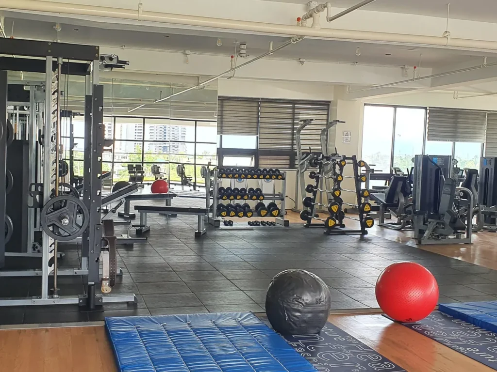 필리핀 세부 CIA어학원 헬스장 바닥에 메디신볼과 짐볼, 매트가 놓이고 뒤로 머신과 덤벨 랙이 늘어서 있다.