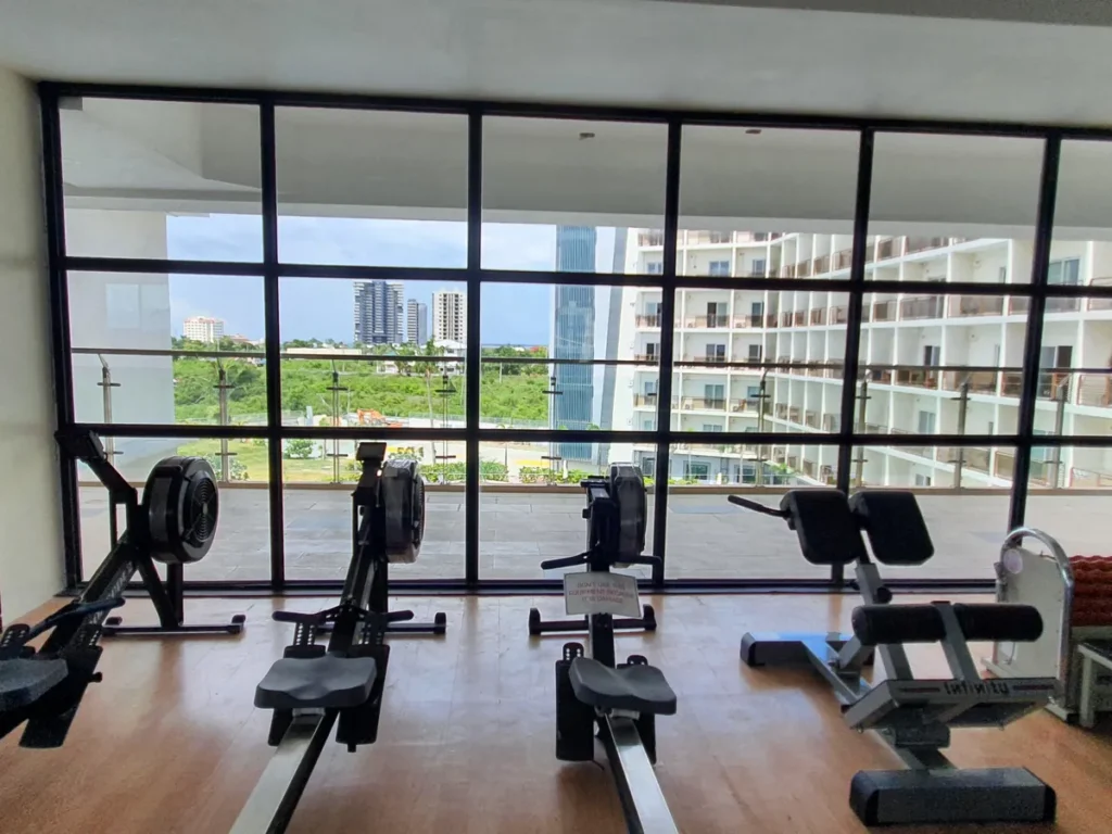 필리핀 세부 CIA어학원 헬스장 통창 앞으로 로잉머신과 백 익스텐션 벤치가 놓여 도심과 건물이 내다보인다.