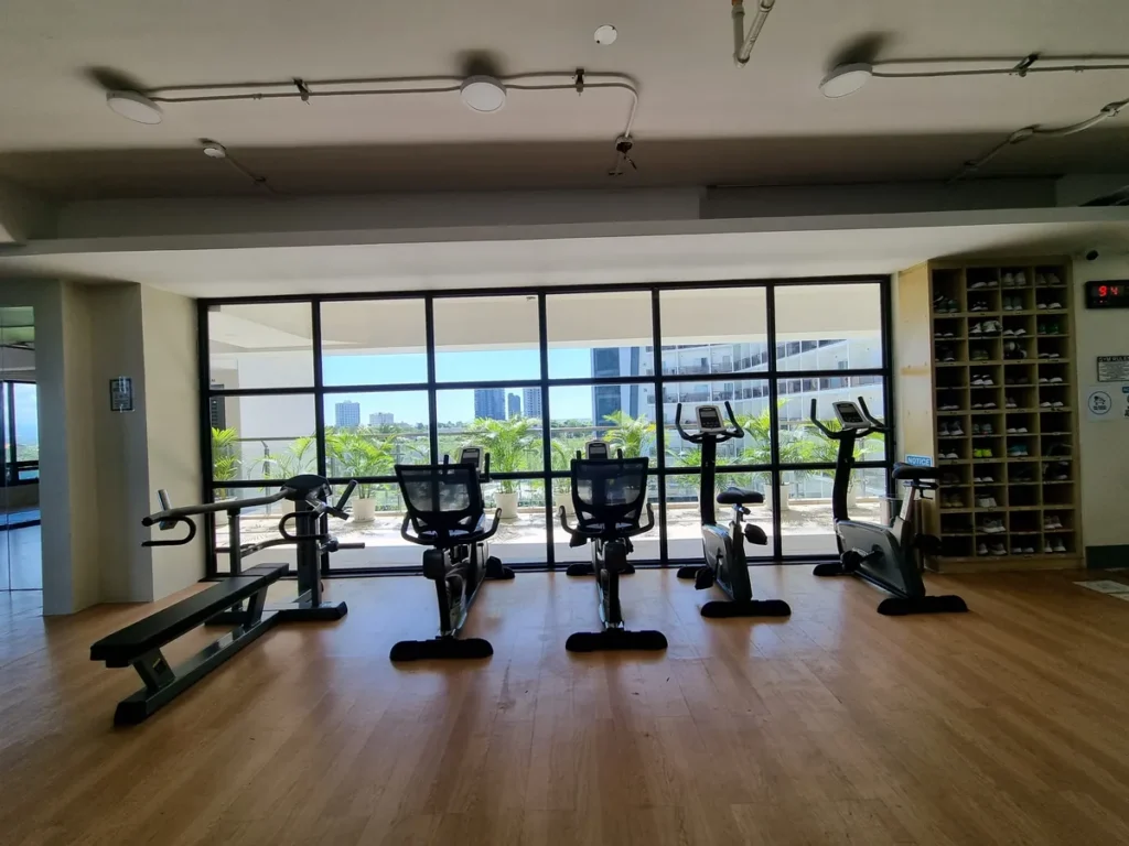 필리핀 세부 CIA어학원 헬스장으로 통창 앞에 실내 자전거와 벤치가 놓이고 한쪽에 신발 보관 선반이 있다.