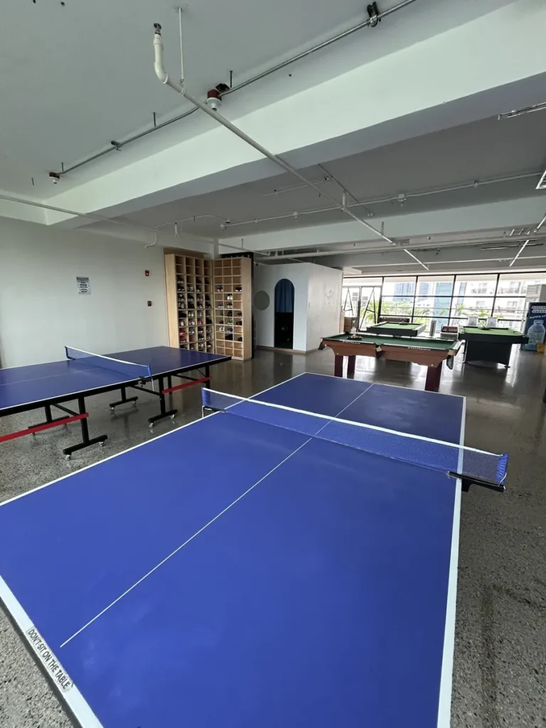 필리핀 세부 CIA어학원 탁구장 전경으로 파란 탁구대 두 대와 안쪽 당구대, 큰 창문, 한쪽 벽 신발 수납장이 보인다