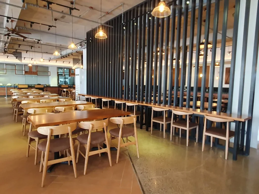 필리핀 세부 CIA어학원 식당 천장 배관과 트랙 조명, 세로 격자 칸막이를 따라 길게 이어진 원목 식탁 좌석