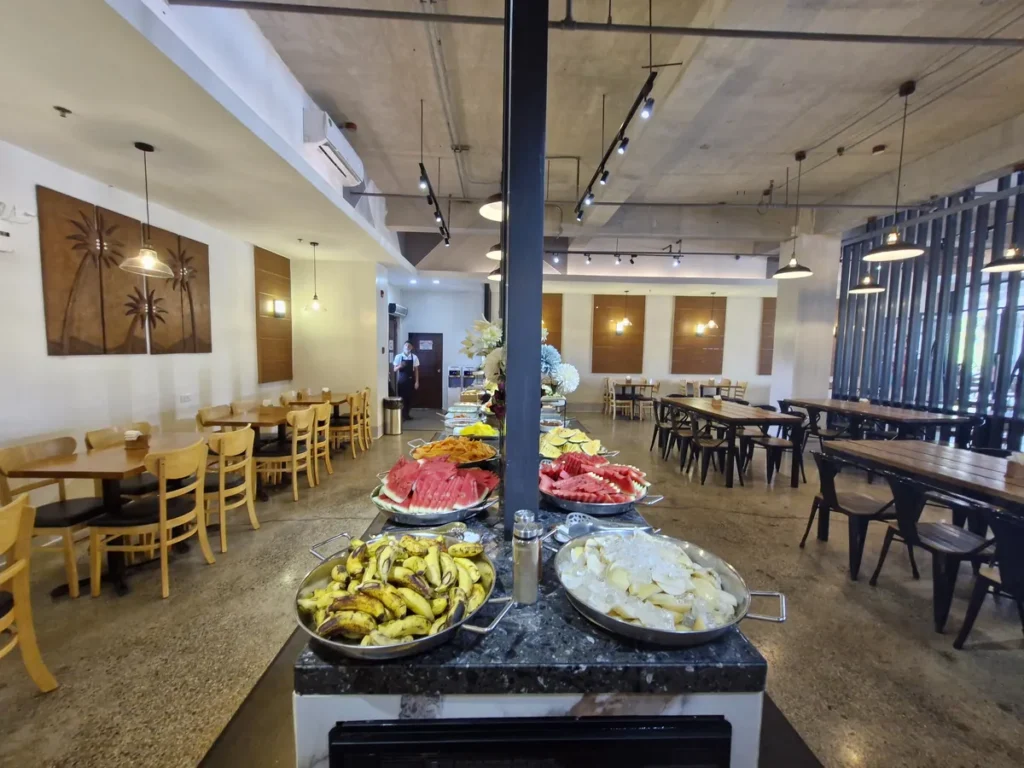 필리핀 세부 CIA어학원 식당 과일 코너, 중앙 대리석 단에 수박과 바나나 등 과일이 큰 접시에 담겨 차려진 모습