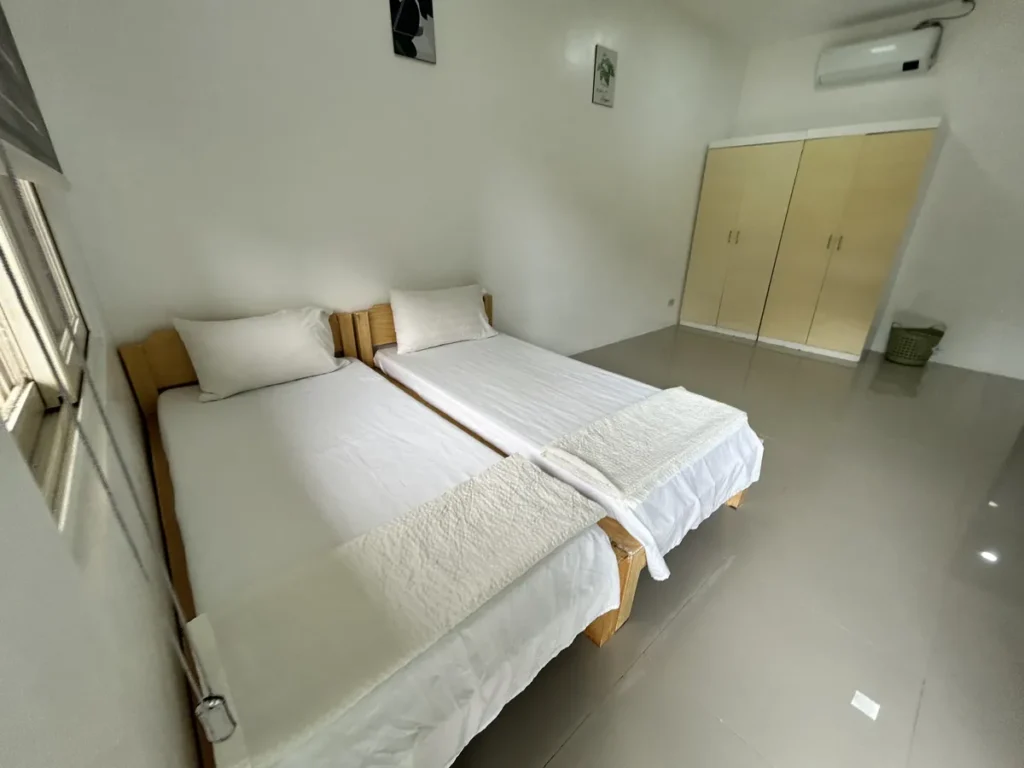필리핀 클락 벨라(BELA) 어학원 기숙사 2인실로, 창가에 붙어있는 원목 침대 두 개와 안쪽의 크림색 옷장, 에어컨이 보이는 넓은 방입니다.