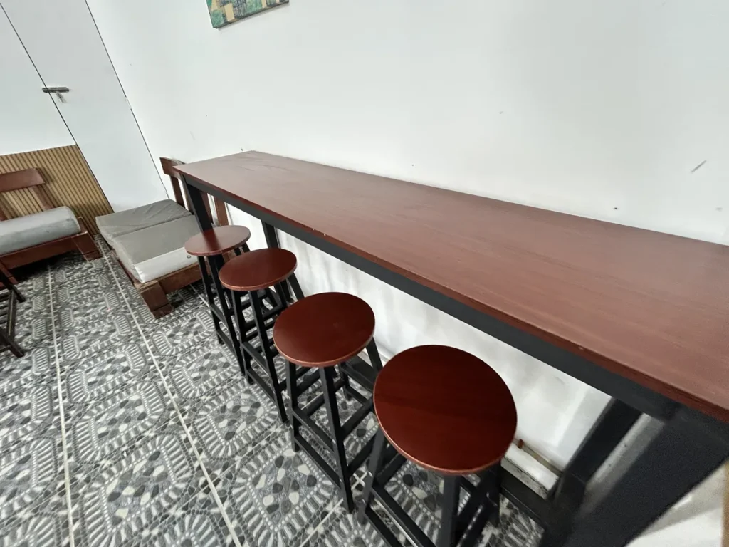필리핀 클락 벨라(BELA) 어학원 부대시설 매점으로, 흰 벽을 따라 놓인 긴 원목 바 테이블과 둥근 원목 스툴 네 개가 나란히 놓인 좌석입니다.