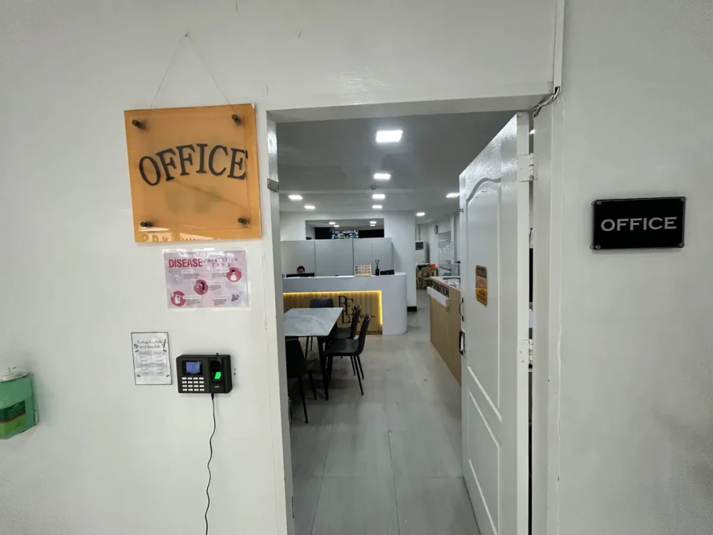 필리핀 클락 벨라(BELA) 어학원 부대시설 오피스로, 벽에 걸린 OFFICE 표지판과 열린 문 너머로 리셉션 데스크가 보이는 사무실 입구 모습입니다.