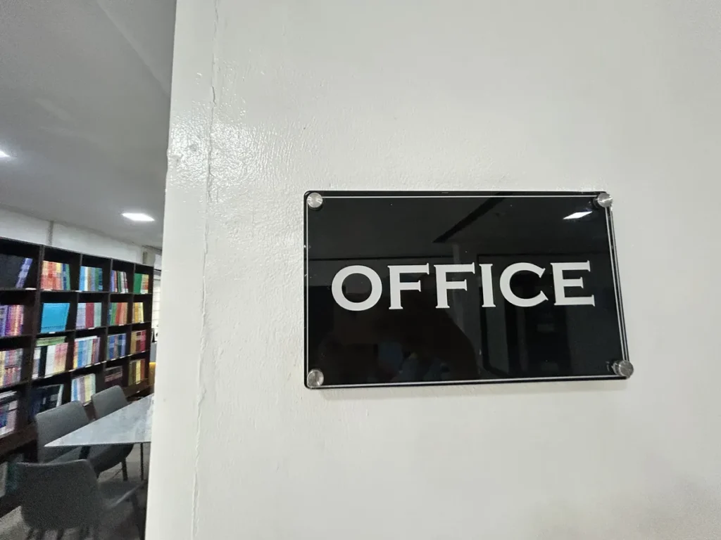 필리핀 클락 벨라(BELA) 어학원 부대시설 오피스로, 흰 벽에 부착된 검정 아크릴 소재 OFFICE 명패를 가까이서 찍은 모습입니다.
