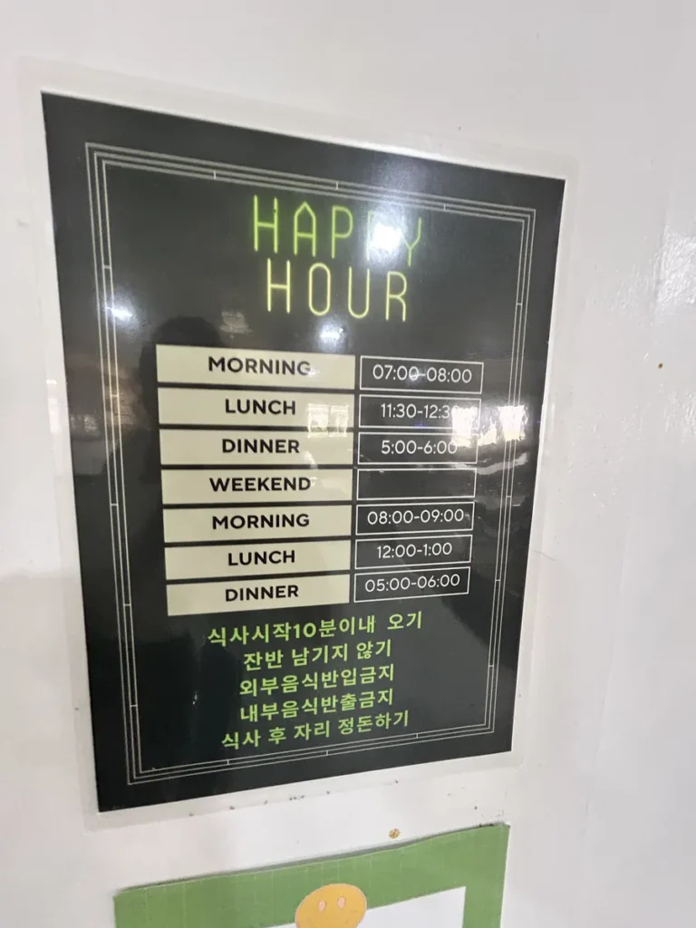 필리핀 클락 벨라(BELA) 어학원 부대시설 안내판으로, 평일·주말 조식·중식·석식 시간표와 식사 예절 안내문이 적힌 Happy Hour 게시판입니다.
