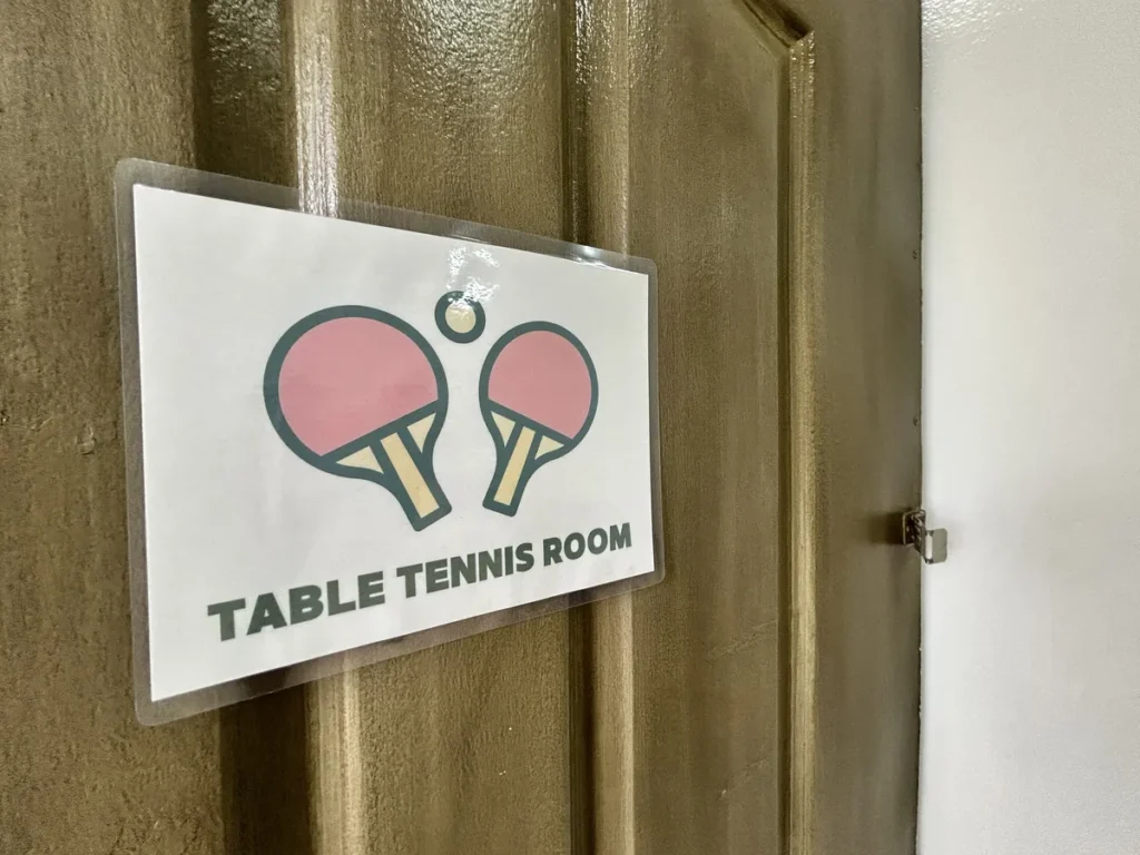 필리핀 클락 벨라(BELA) 어학원 운동시설 탁구장으로, 나무 문에 라켓 그림과 TABLE TENNIS ROOM 표지판이 붙어 있는 모습입니다.