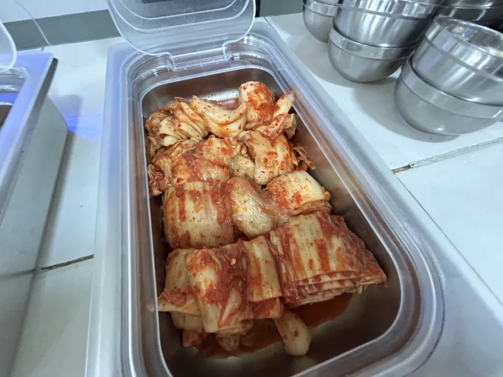 필리핀 클락 벨라(BELA) 어학원 식당 식사로, 배식통에 빨갛게 양념된 배추김치가 큼직하게 담겨 있습니다.