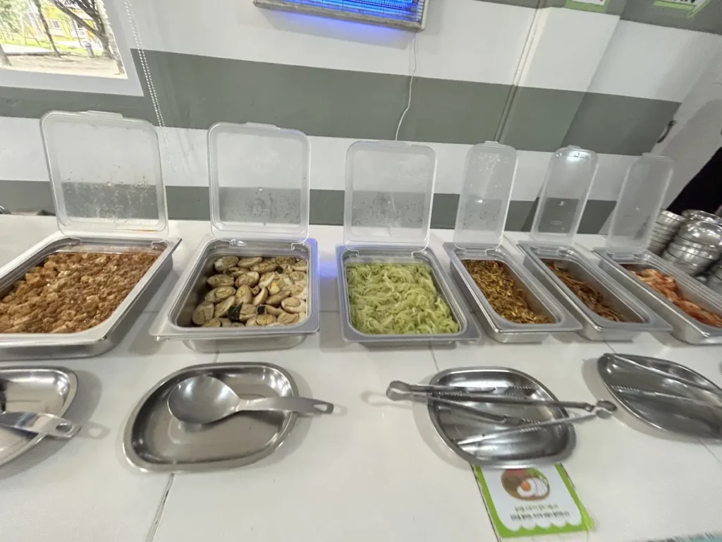 필리핀 클락 벨라(BELA) 어학원 식당 식사로, 뚜껑이 열린 스테인리스 배식통 여러 개가 나란히 놓인 셀프 배식대 모습입니다.