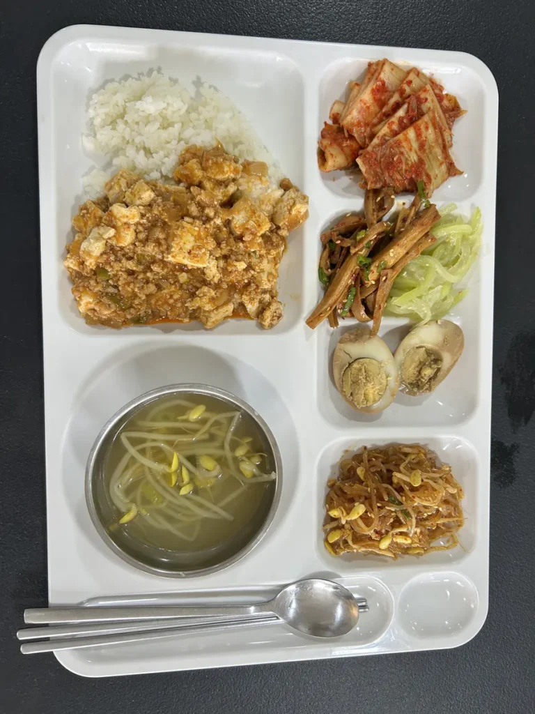 필리핀 클락 벨라(BELA) 어학원 식당 식사로, 흰쌀밥·마파두부·배추김치·우엉조림·오이무침·삶은 계란·잡채·콩나물국이 한 식판에 담긴 모습입니다.