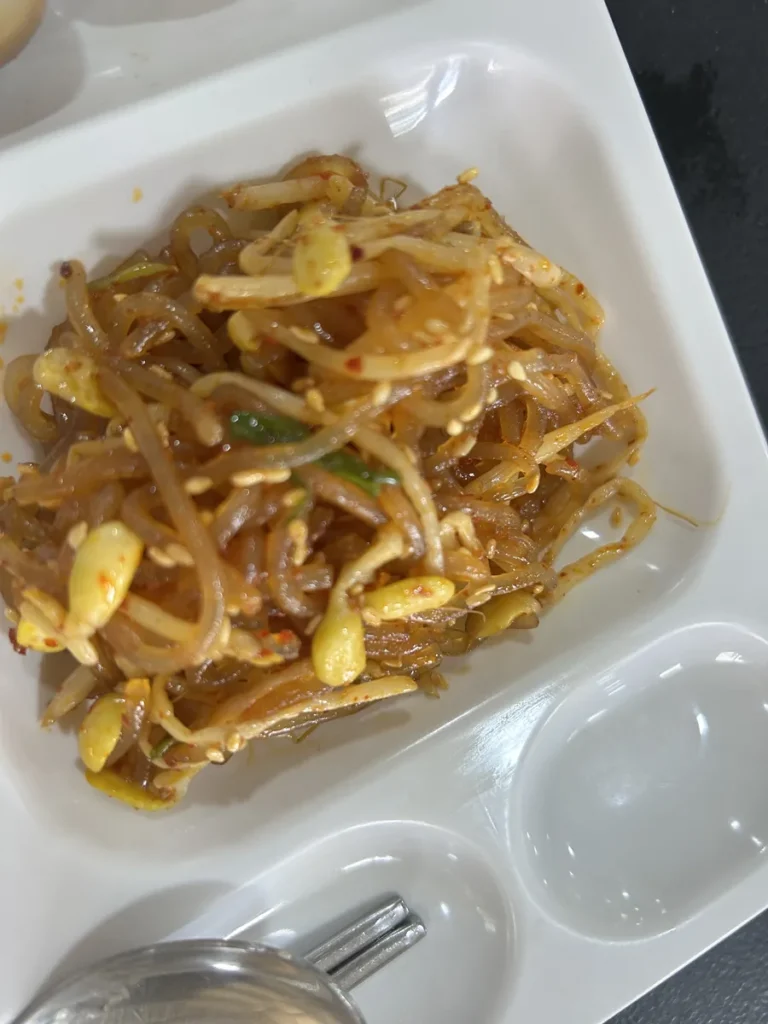 필리핀 클락 벨라(BELA) 어학원 식당 식사로, 식판에 담긴 당면과 콩나물, 참깨·견과가 어우러진 잡채풍 반찬을 가까이서 찍은 모습입니다.