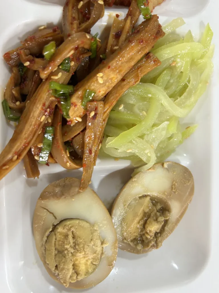 필리핀 클락 벨라(BELA) 어학원 식당 식사로, 식판 위 참깨 뿌린 우엉조림과 오이무침, 반으로 자른 삶은 계란을 가까이서 찍은 모습입니다.