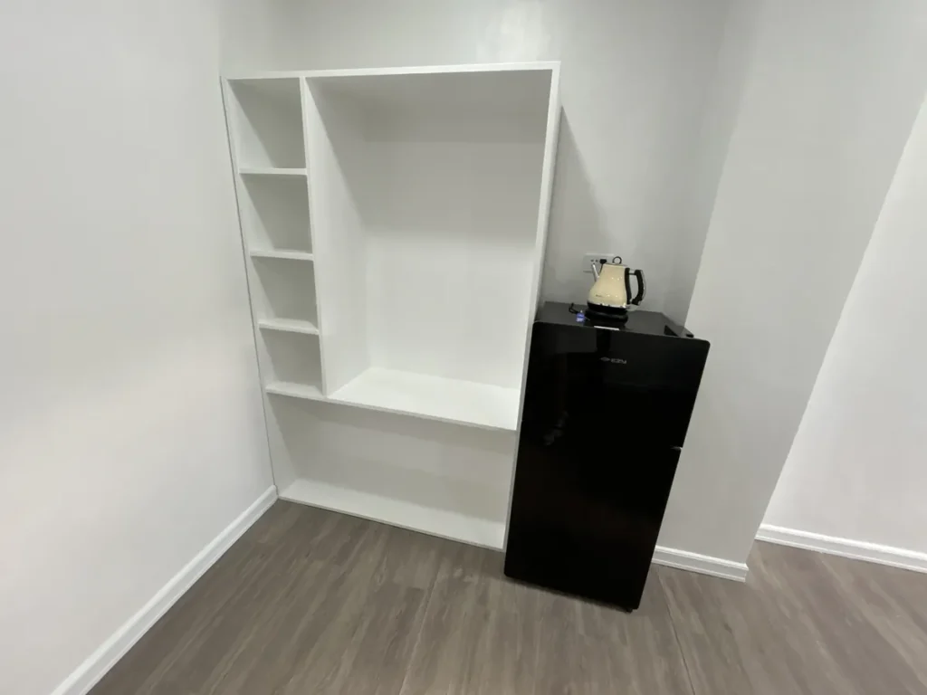 필리핀 세부 바나나키즈(BK) 어학원 기숙사 3인실로, 빈 칸의 흰색 수납 선반장과 그 옆 검은 미니냉장고 위 크림색 전기포트를 가까이서 담았습니다.
