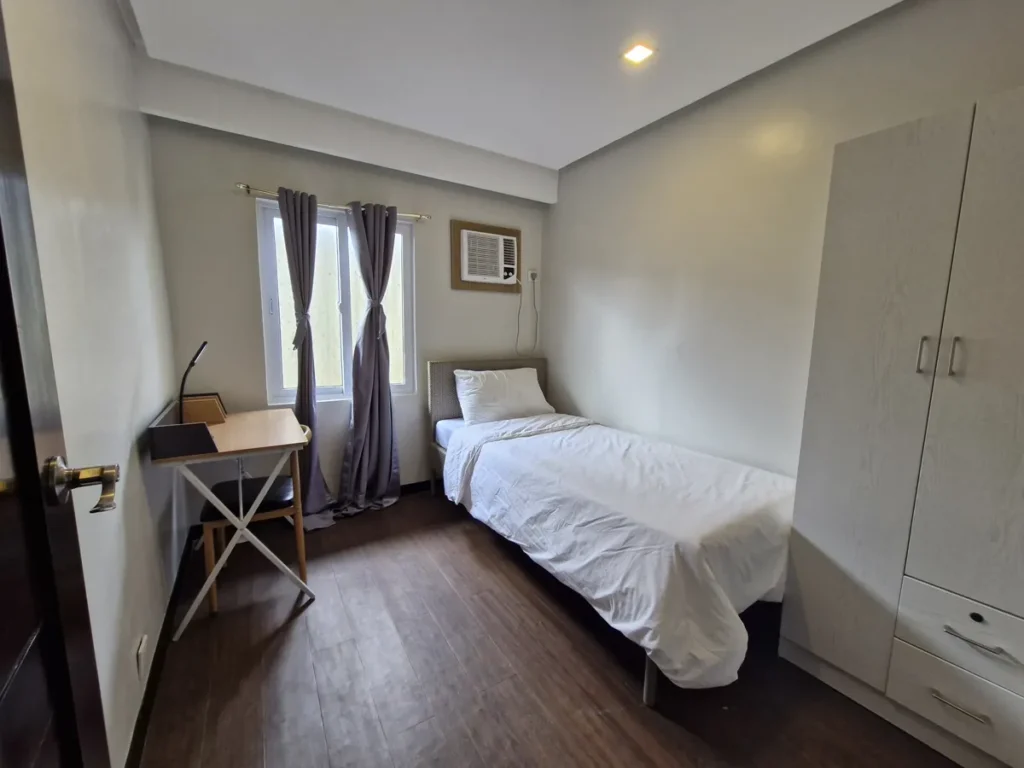 필리핀 세부 바나나키즈(BK) 어학원 외부 독채 기숙사 침실로, 흰색 서랍장 옷장과 접이식 책상이 싱글베드와 함께 놓인 회색 커튼 창가 방입니다.