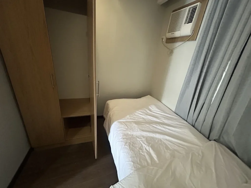 필리핀 세부 바나나키즈(BK) 어학원 외부 독채 기숙사 침실로, 문을 연 우드톤 옷장 내부 선반과 벽걸이 에어컨, 침대 모서리가 함께 보입니다.
