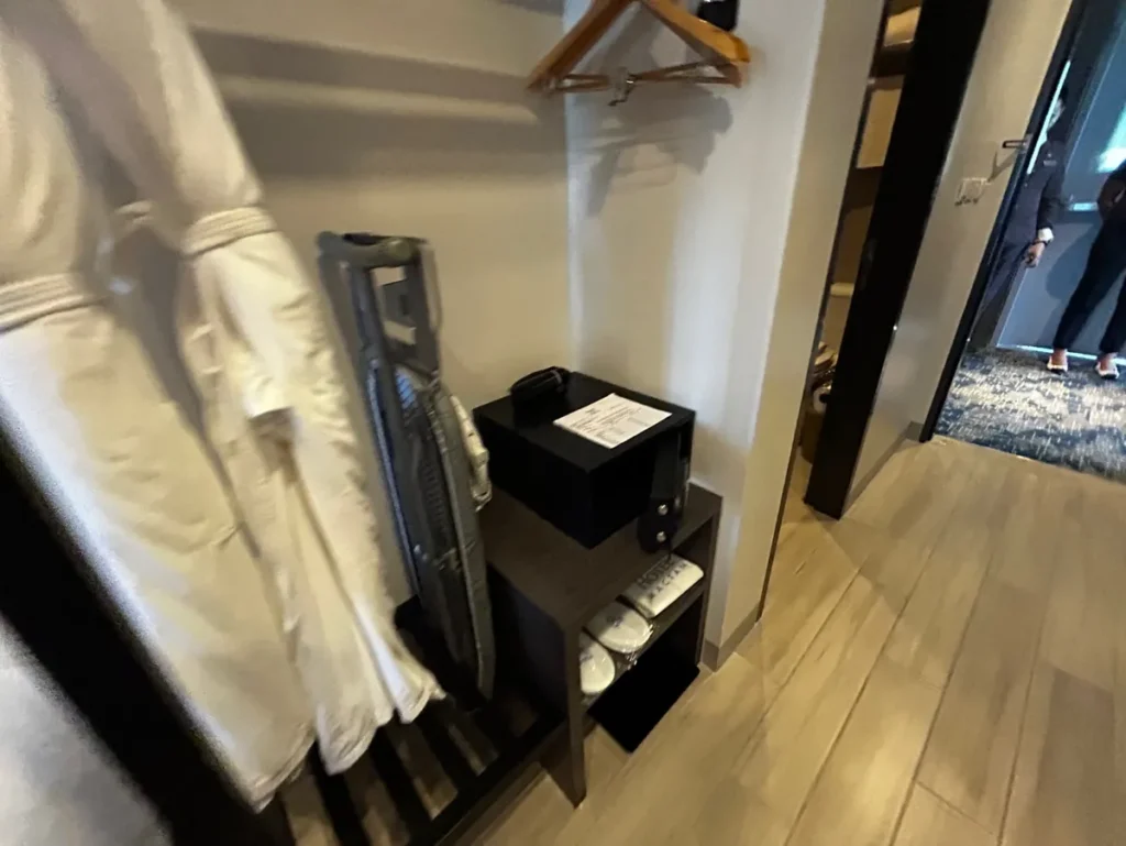 필리핀 세부 바나나키즈(BK) 어학원 외부 호텔 기숙사 객실 수납코너로, 접이식 다림판과 옷걸이 아래 검은 전자 금고가 놓인 공간입니다.