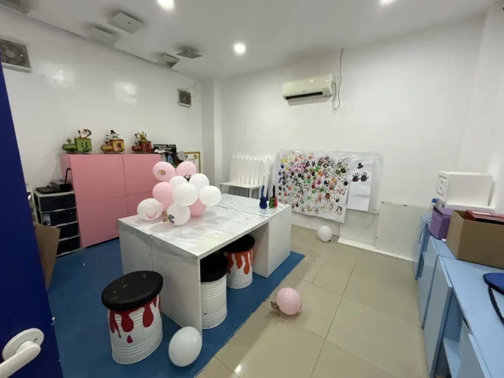 필리핀 세부 바나나키즈(BK) 어학원 키즈룸 미술공작실로, 눈사람 인형과 기차 모형 옆 통조림 스툴과 풍선이 있는 놀이 코너입니다.
