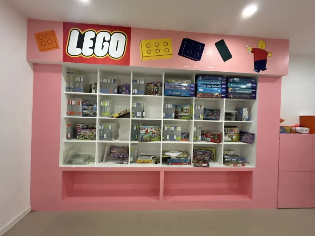 필리핀 세부 바나나키즈(BK) 어학원 키즈룸 레고룸으로, 빨간 LEGO 간판 아래 분홍 선반에 레고 교구 상자가 정리된 모습입니다.
