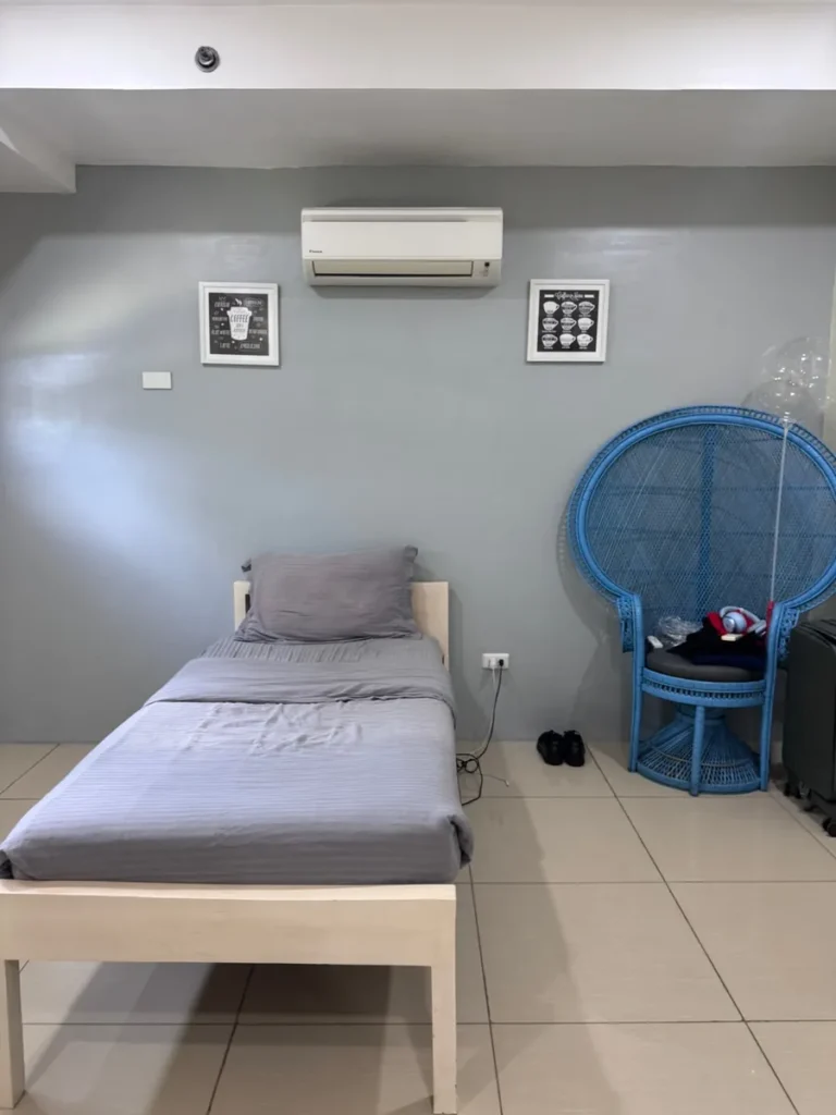 필리핀 세부 셀라(CELLA) 유니캠퍼스 어학원 기숙사 1인실로, 그레이 침구의 싱글 침대와 에어컨, 액자 장식이 놓인 아늑한 침실 공간입니다.